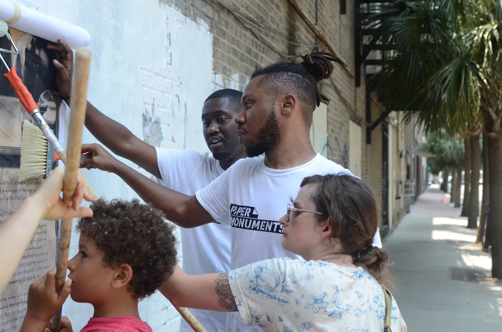  Paper Monuments co-director Bryan Lee, team member Nic Aziz, and volunteer Dana install posters at the Elk Place site.  