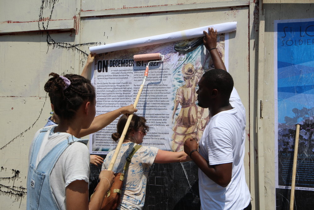  Paper Monuments volunteers Erica and Dana and co-director Bryan Lee Jr. install PMEV#023 Farewell to the Honorable Marcus Garvey at the Rampart Street site.  