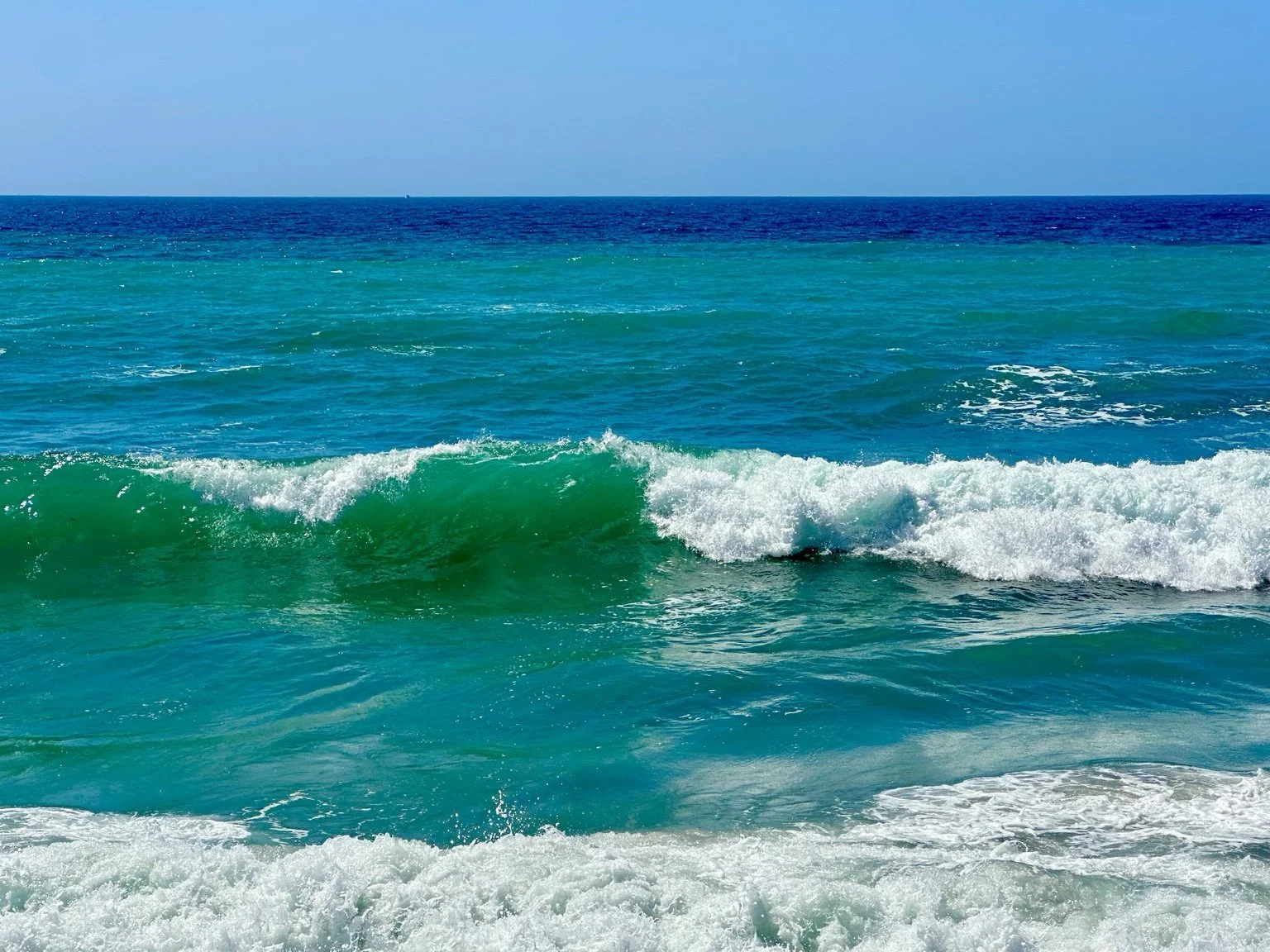 Turquoise ocean waves breaking along the coast, photographed by Traci.