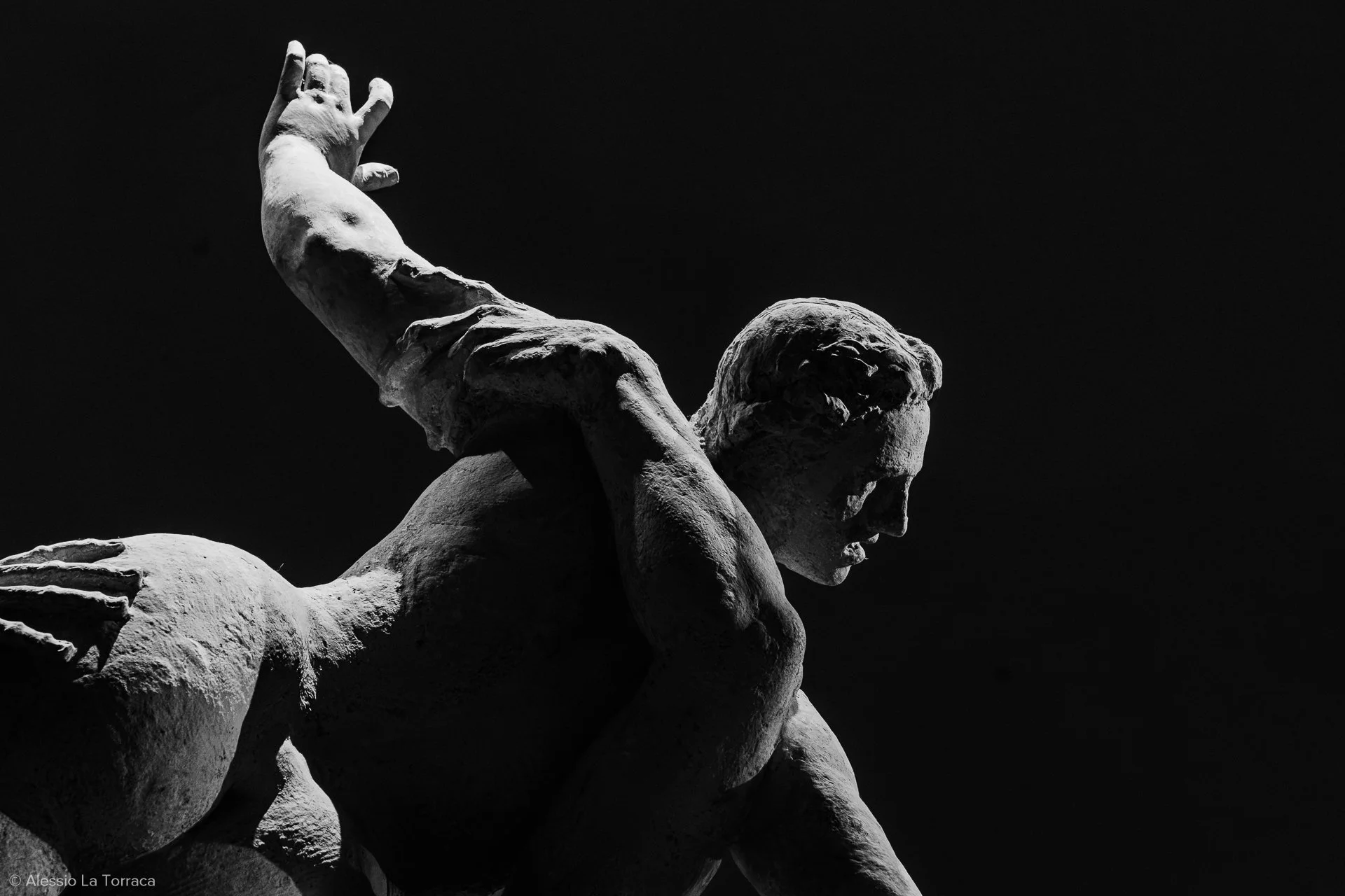 Black and white photo of a classical statue of a woman in profile, with a dark background.
