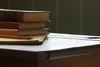 A stack of books and a notepad with a pencil on a wooden desk