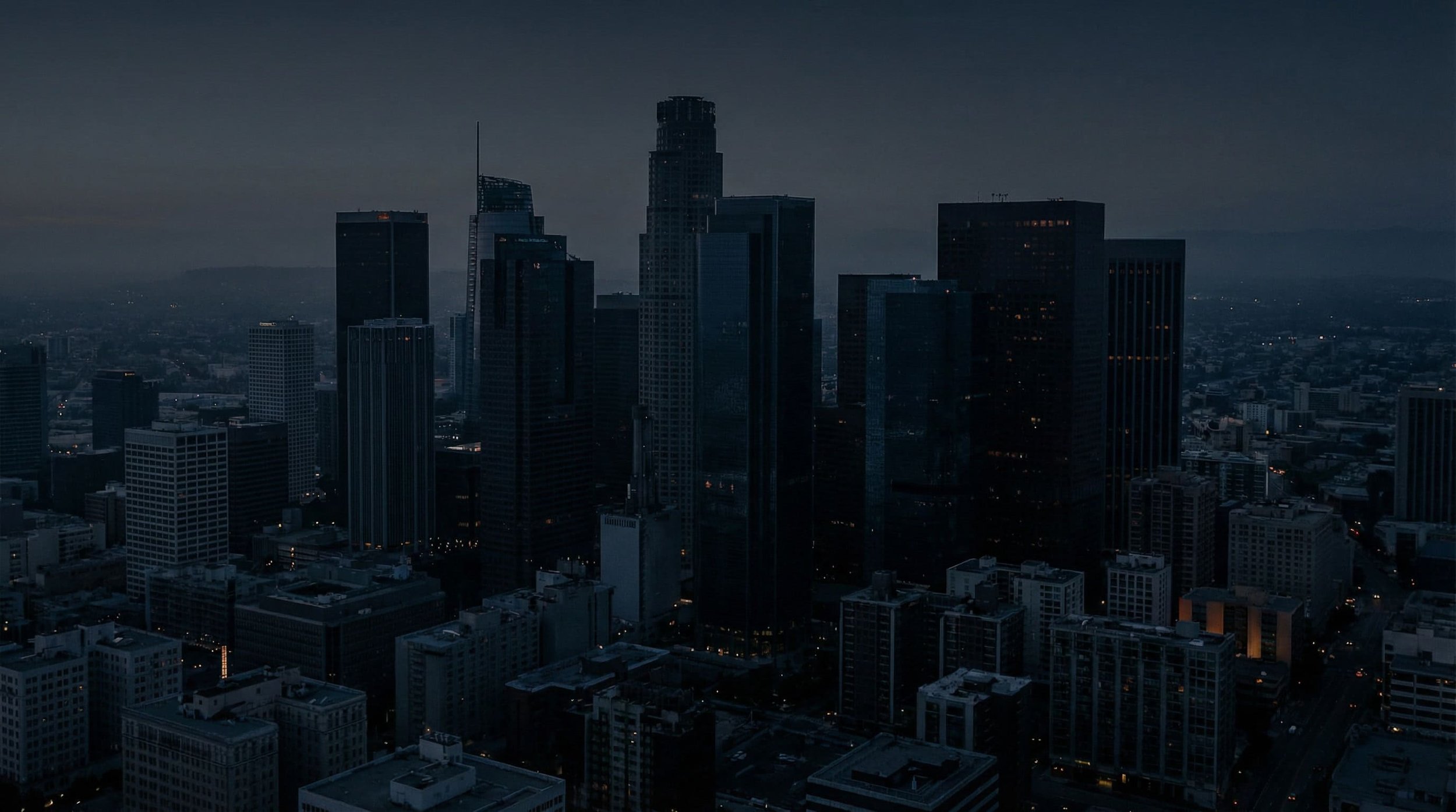 Aerial view of the Los Angeles skyline at dusk, with high-rise buildings under a dark blue sky.