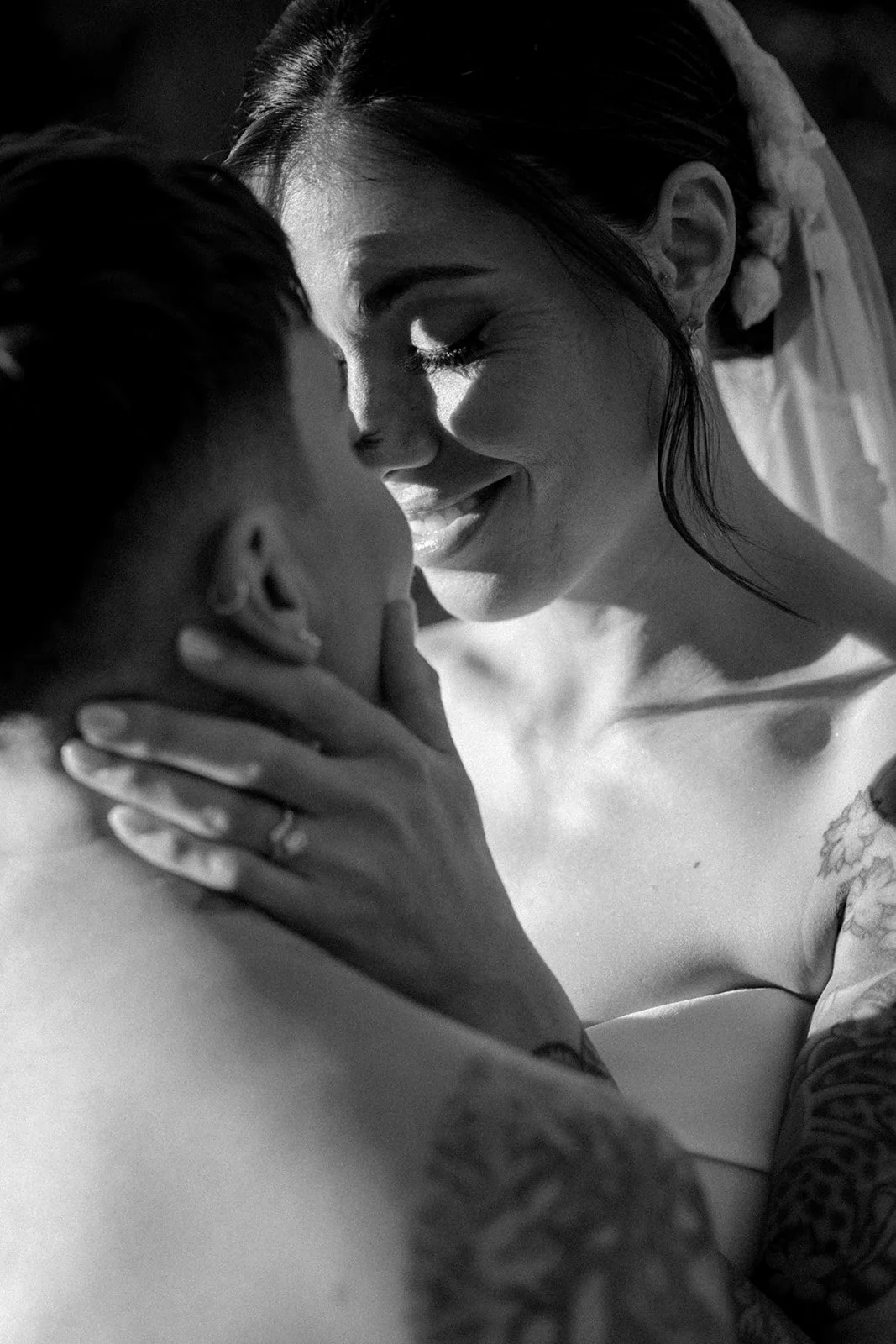 Black and white photo of a bride and groom in a close embrace, smiling softly with their faces close together.