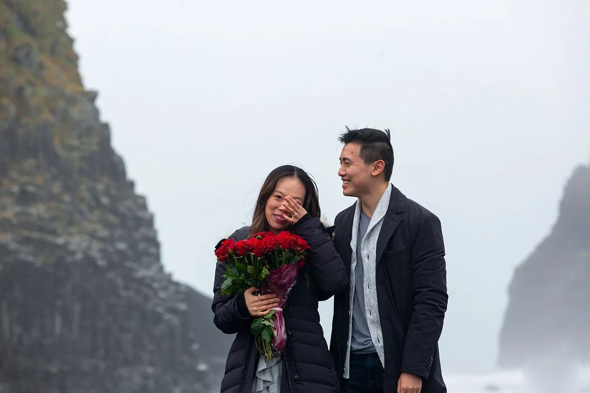 Woman is emotional and happy after a surprise proposal at the black beach in Iceland. He gave her a dozen red roses.
