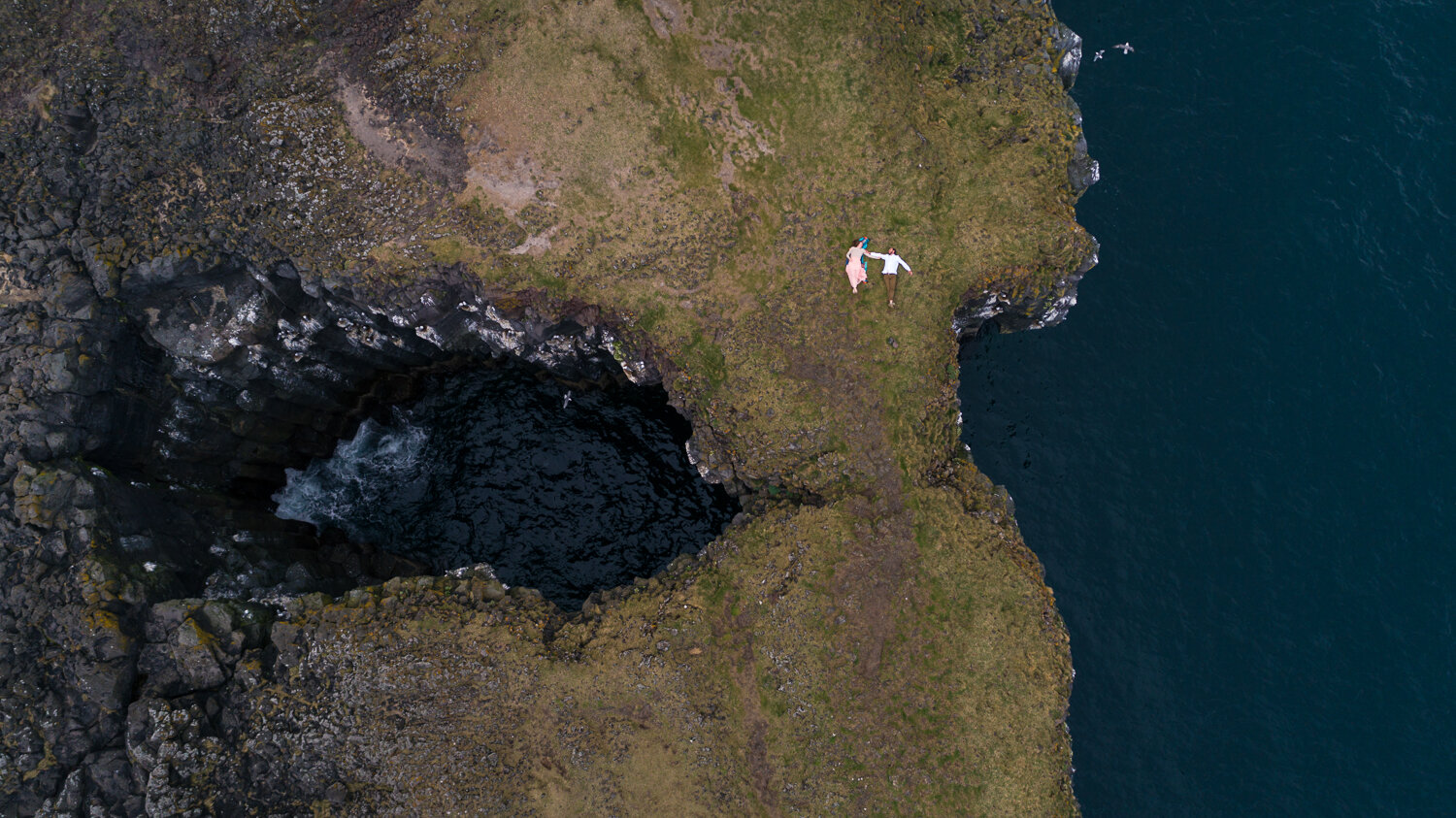 Iceland elopement photographer. Drone elopement photography of a couple on rock arch bridge over ocean at Arnarstapi in Iceland.