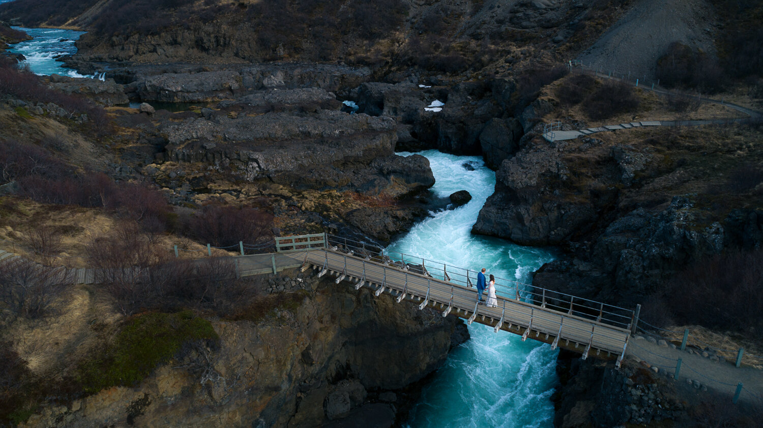 Iceland elopement photographer. Drone elopement photography of a couple on a bridge over Hraunfossar and barnafoss waterfall in Iceland.