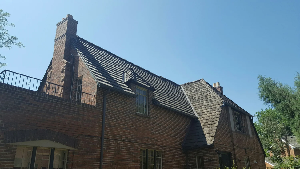 Brick home with a steep gambrel roof design, dormer windows, and a prominent chimney under a clear blue sky.
