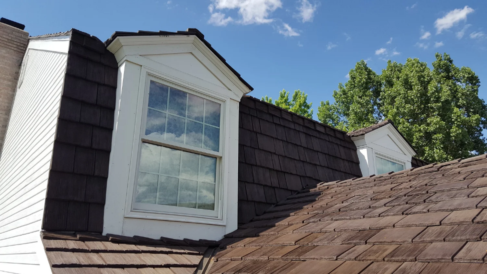 Dormer window on a shingle roof highlighting a gambrel roof design with white trim and wood shingles.