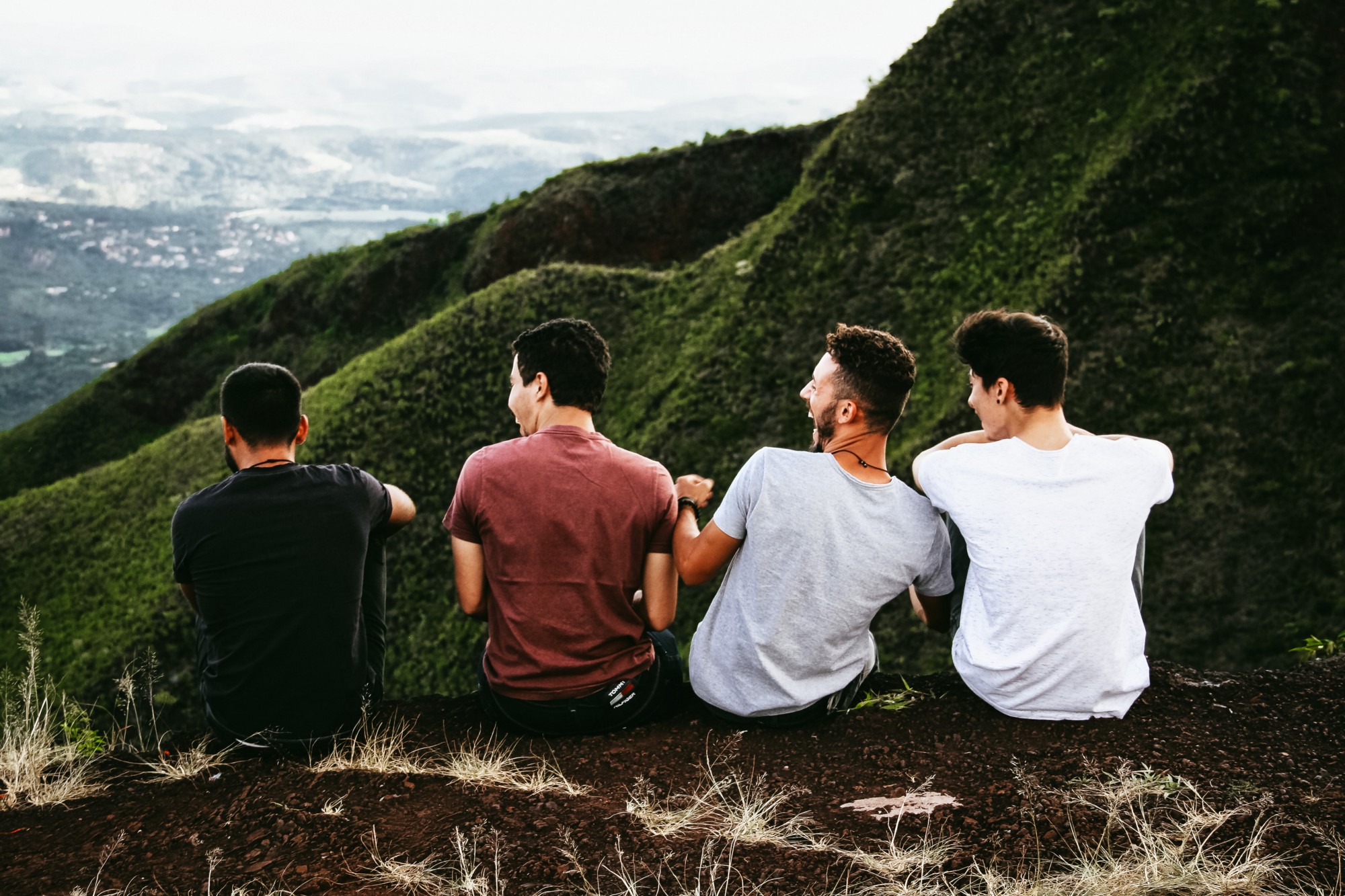 “A group of four laughing men sits on an edge overlooking a green valley” by Matheus Ferrero on Unsplash