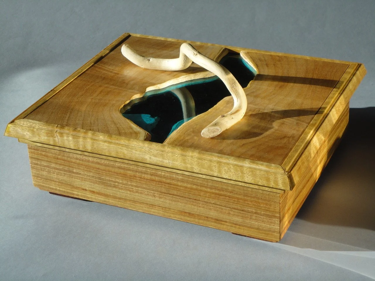   Blue Lagoon Box , Matthew X. Curry,  Figured maple with inlaid blue glass and waxed willow top, trimmed with figured movinque. Canary wood sides, paduak feet and maple liner,  8.5” x  9.75” x  3.25” $625                      ‍ 