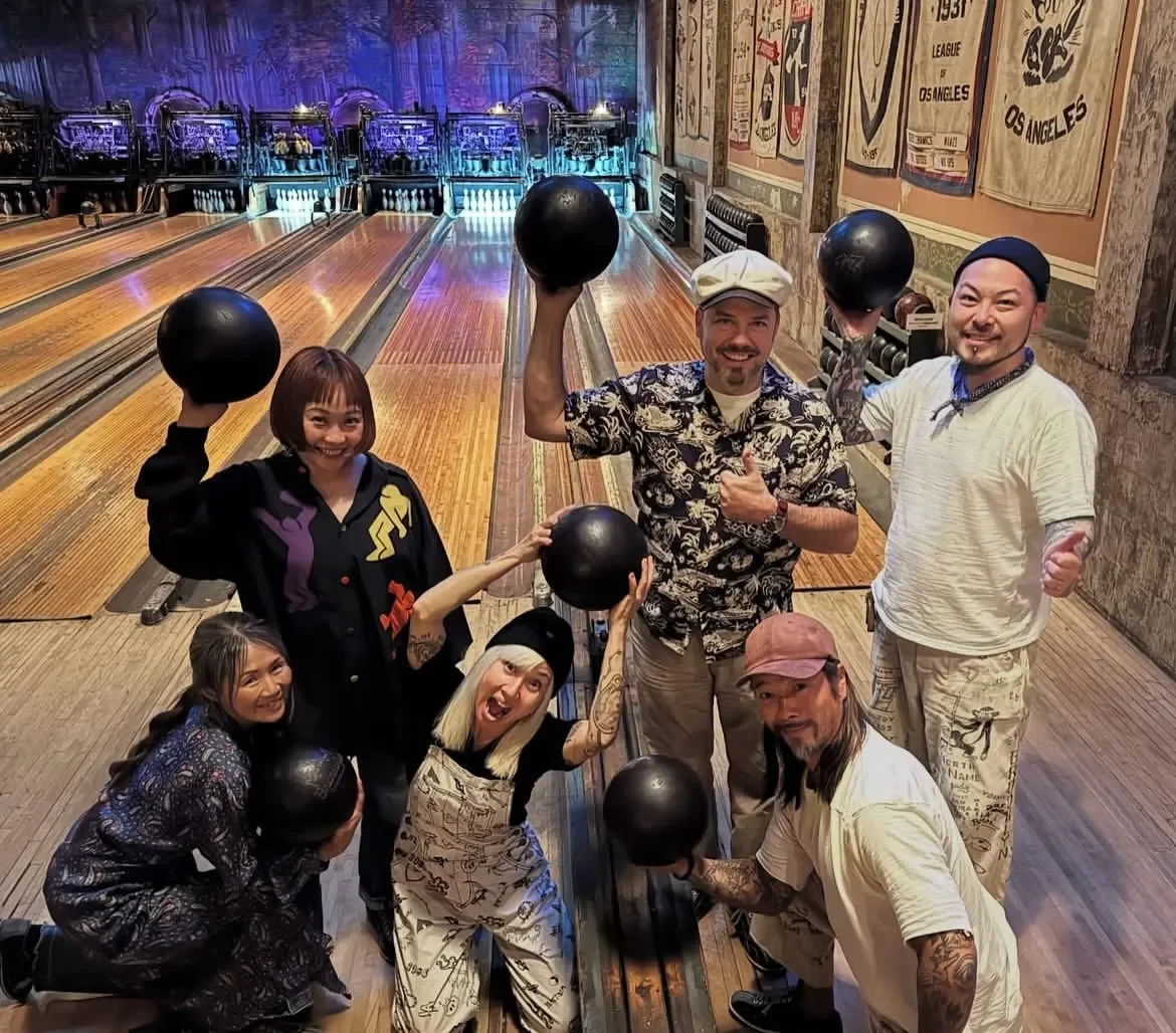 A happy group of friends holding bowling balls on the lanes at Highland Park Bowl.