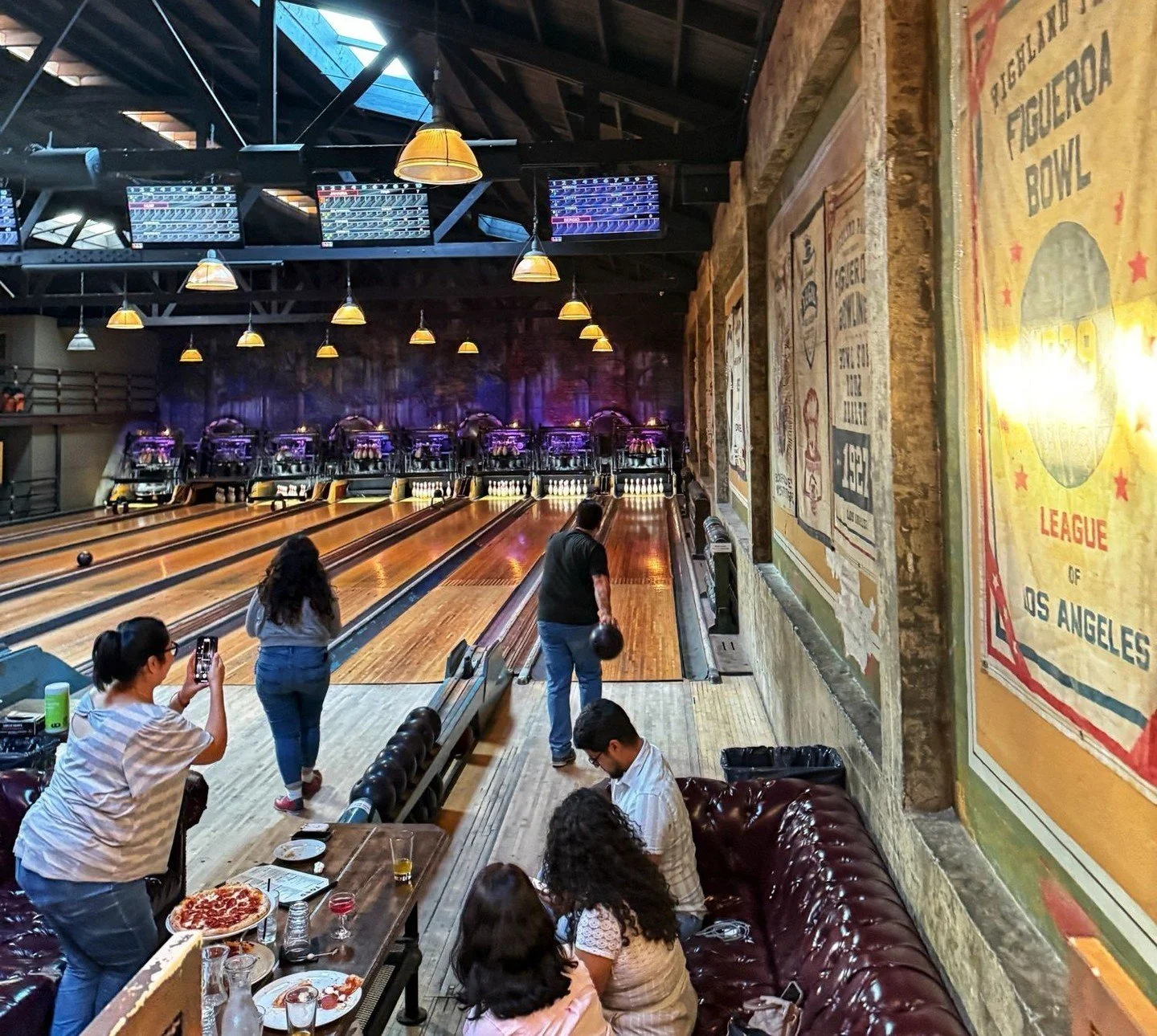 Historic bowling lanes at Highland Park Bowl with people playing and food on the table.