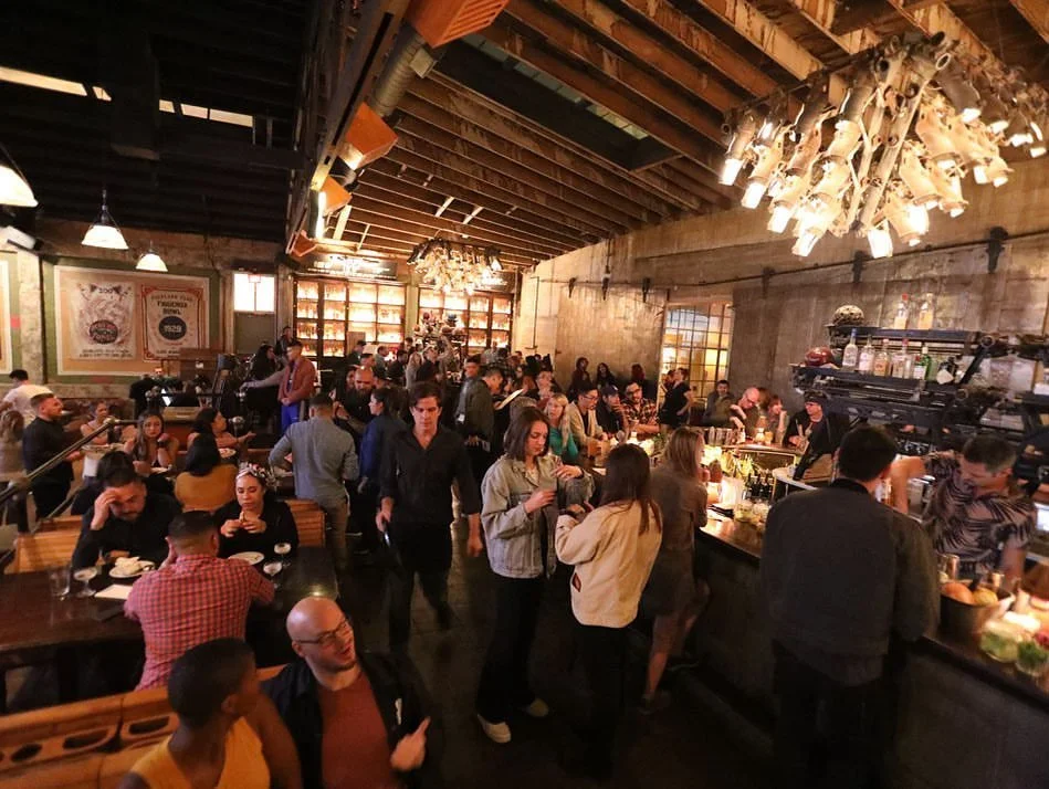 Guests enjoying craft cocktails and conversation around the lively bar and bowling lanes inside Highland Park Bowl in Los Angeles.
