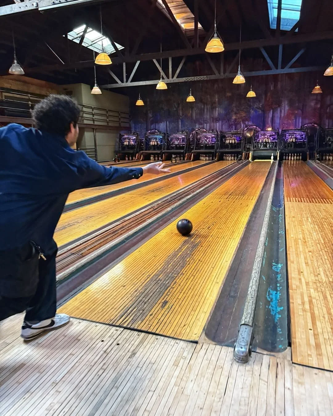 A person bowls a ball down a wooden lane at the vintage Highland Park Bowl.