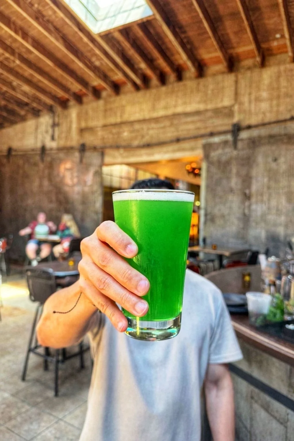 Person holding a bright green cocktail at Highland Park Bowl during a lively summer evening.