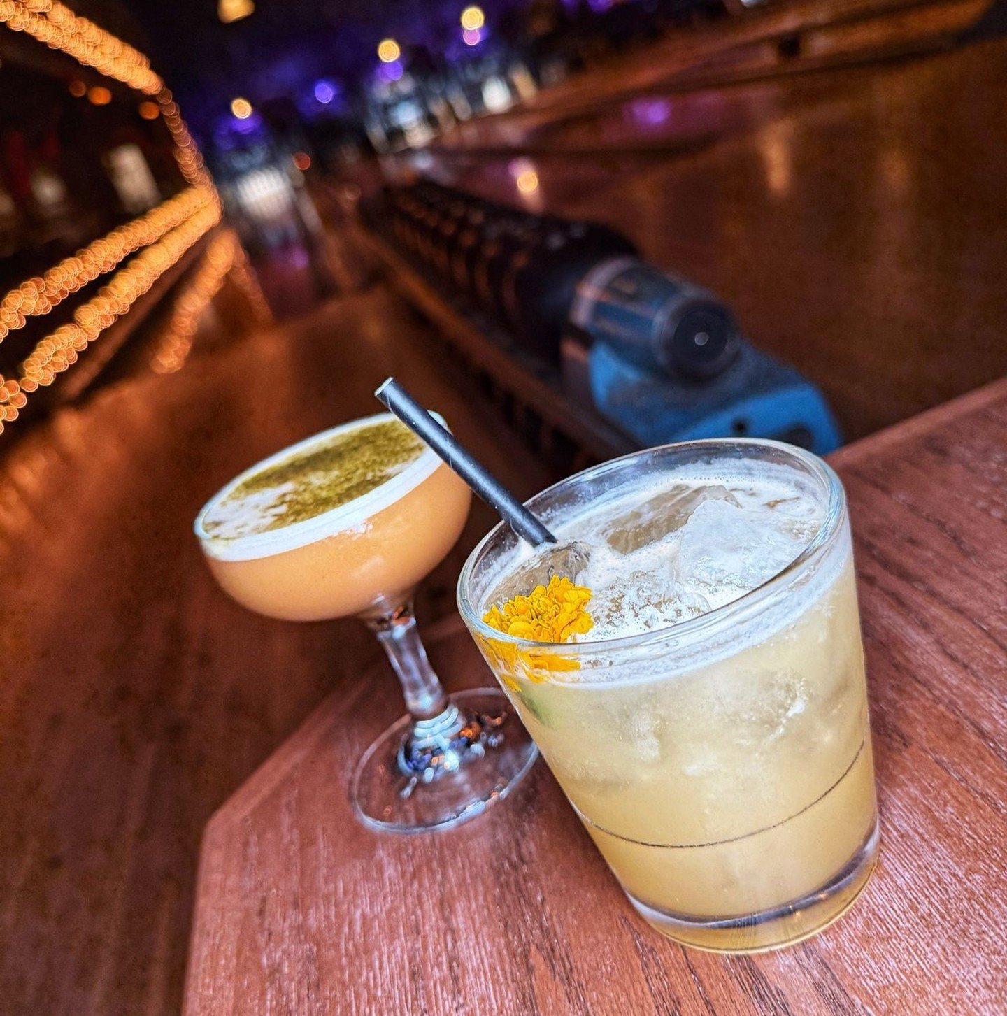 Cocktails placed by a bowling lane at Highland Park Bowl with warm lights and blurred alley in the background.