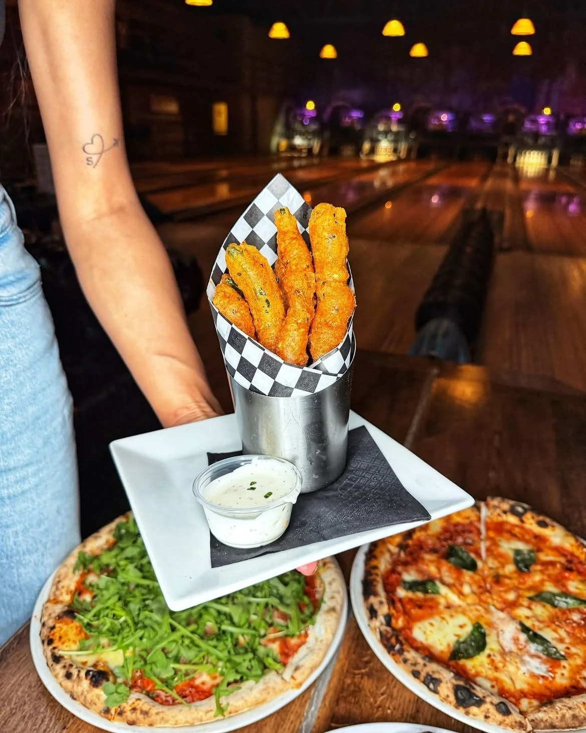 Crispy fried appetizers served in a metal cone alongside two freshly baked pizzas on a table at Highland Park Bowl.