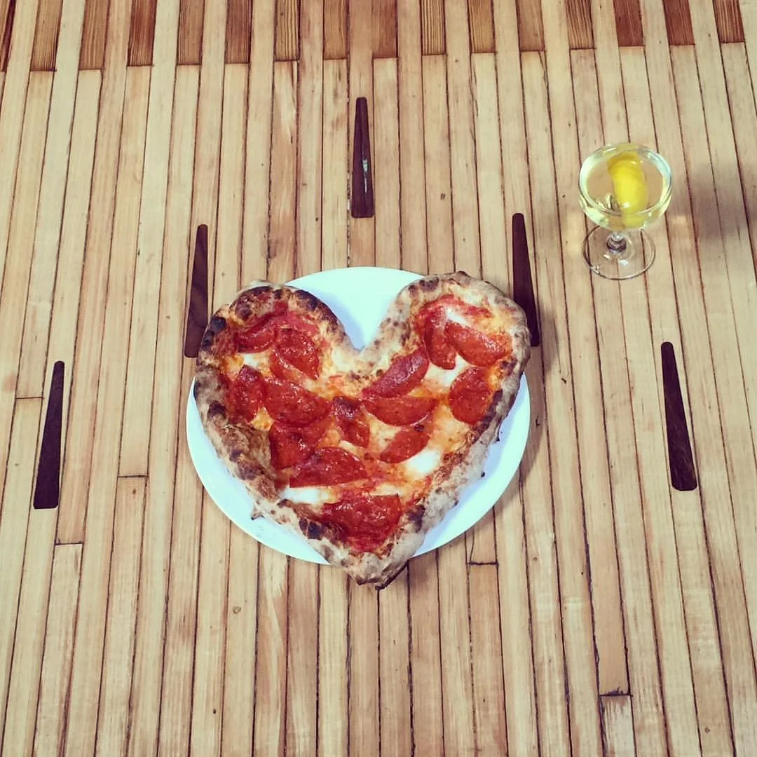 A heart-shaped pepperoni pizza and cocktail served beside a vintage bowling lane at Highland Park Bowl.