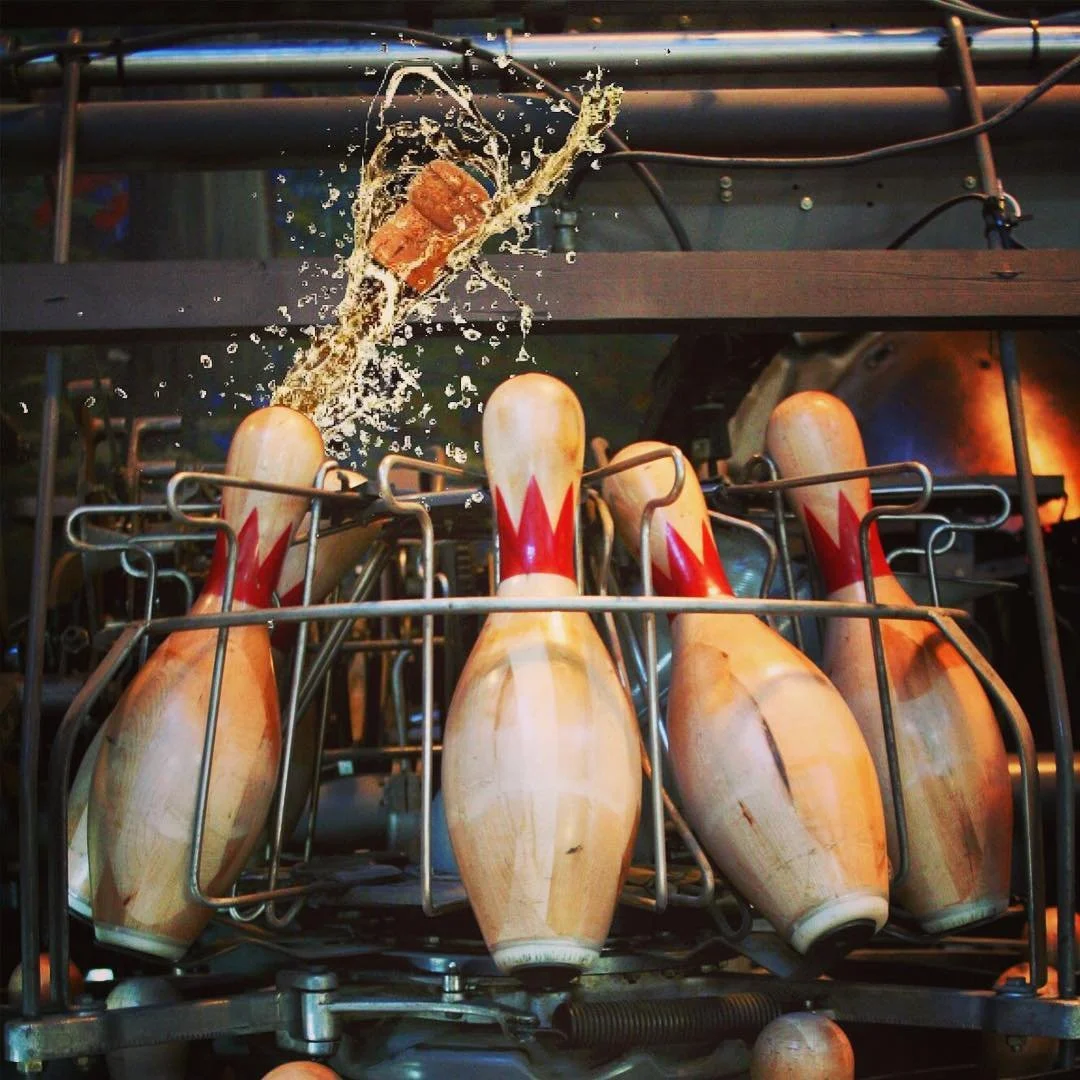 Bowling pins set in a machine with a drink bursting around a flying cork from Highland Park Bowl.
