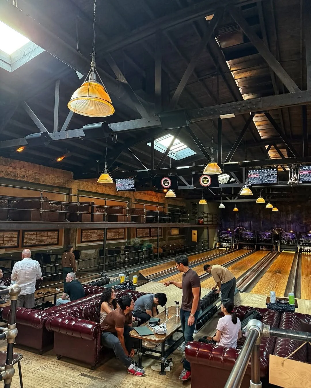 A group of people sitting on maroon couches and bowling at Highland Park Bowl.
