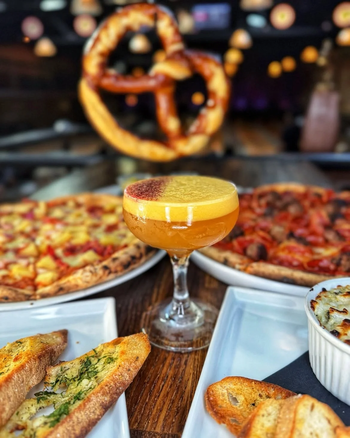 Signature cocktail served with pizza, garlic bread, and a large pretzel at Highland Park Bowl.