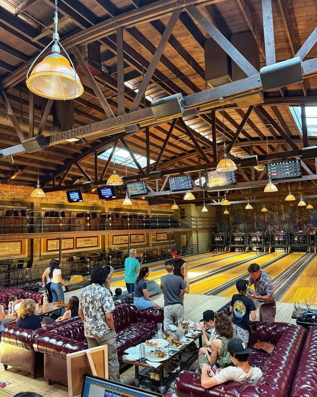 Group of friends and family relaxing and socializing on vintage maroon leather couches beside the bowling lanes at Highland Park Bowl.