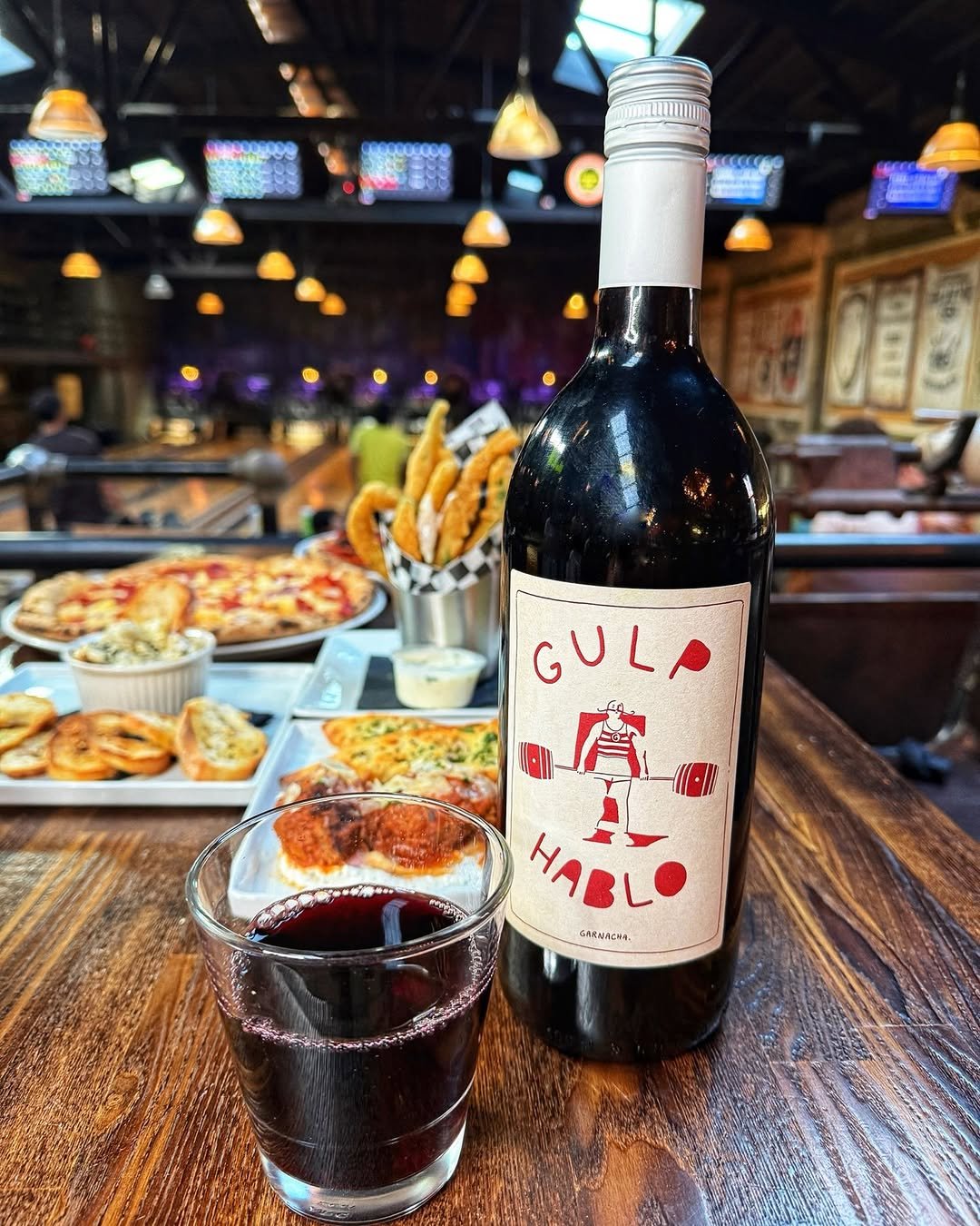 Bottle of Gulp Hablo wine served with appetizers on a lane-side table overlooking the bowling alley at Highland Park Bowl.