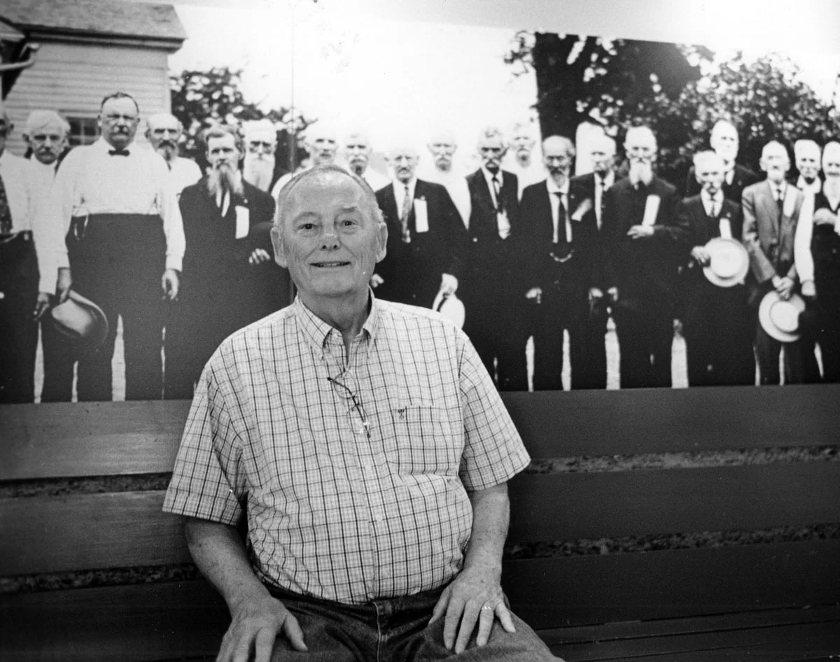 Inside the museum, Lou Wagner poses next to the image of his grandfather, Sgt. Timothy Metzler, in a mural print of a photo of a reunion of 103rd O.V.I. veterans.
