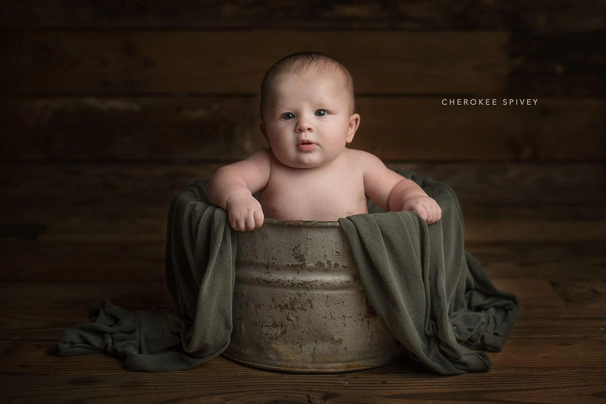 Chunky five month old baby sits in a rustic old washtub sitting on a wooden porch.
