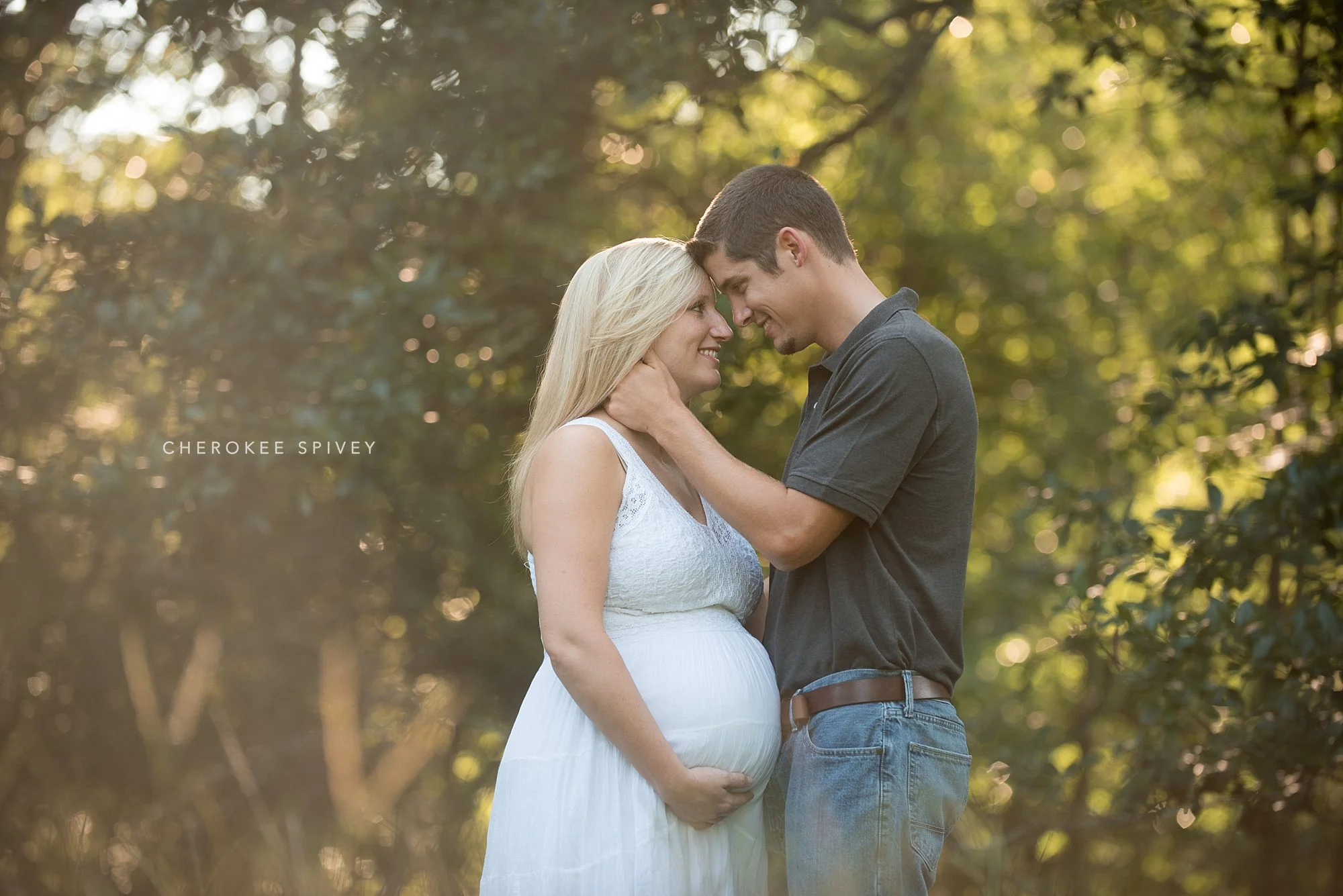lush green foliage is the backdrop for a handsome couple gazing into the others' eyes as she displays her large belly