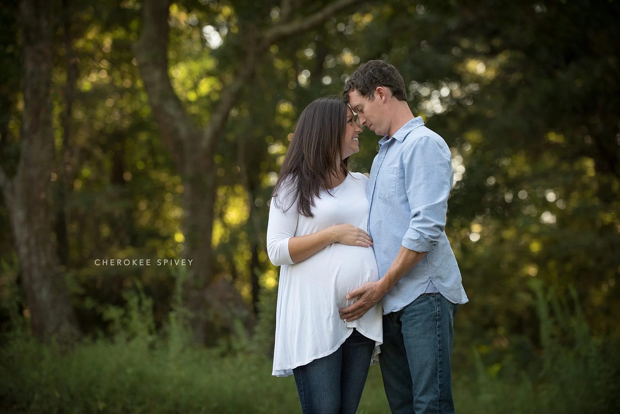 Young couple affectionately cuddling while holding the woman's pregnant belly in the edge of a forest