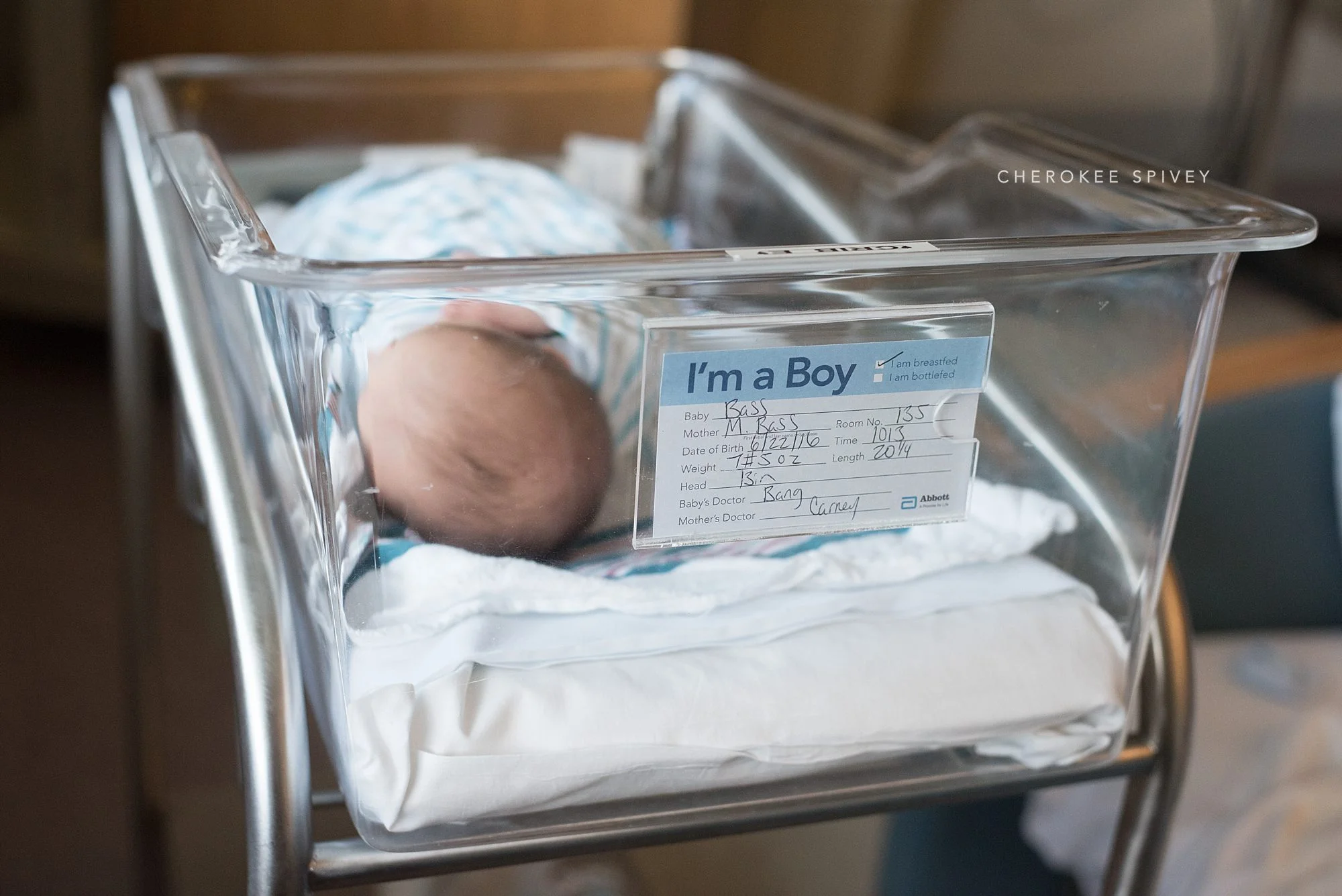 A see-through bassinet with a tag giving the baby boy's dob, weight, name, etc. and you can see the top of the baby's head next to it.