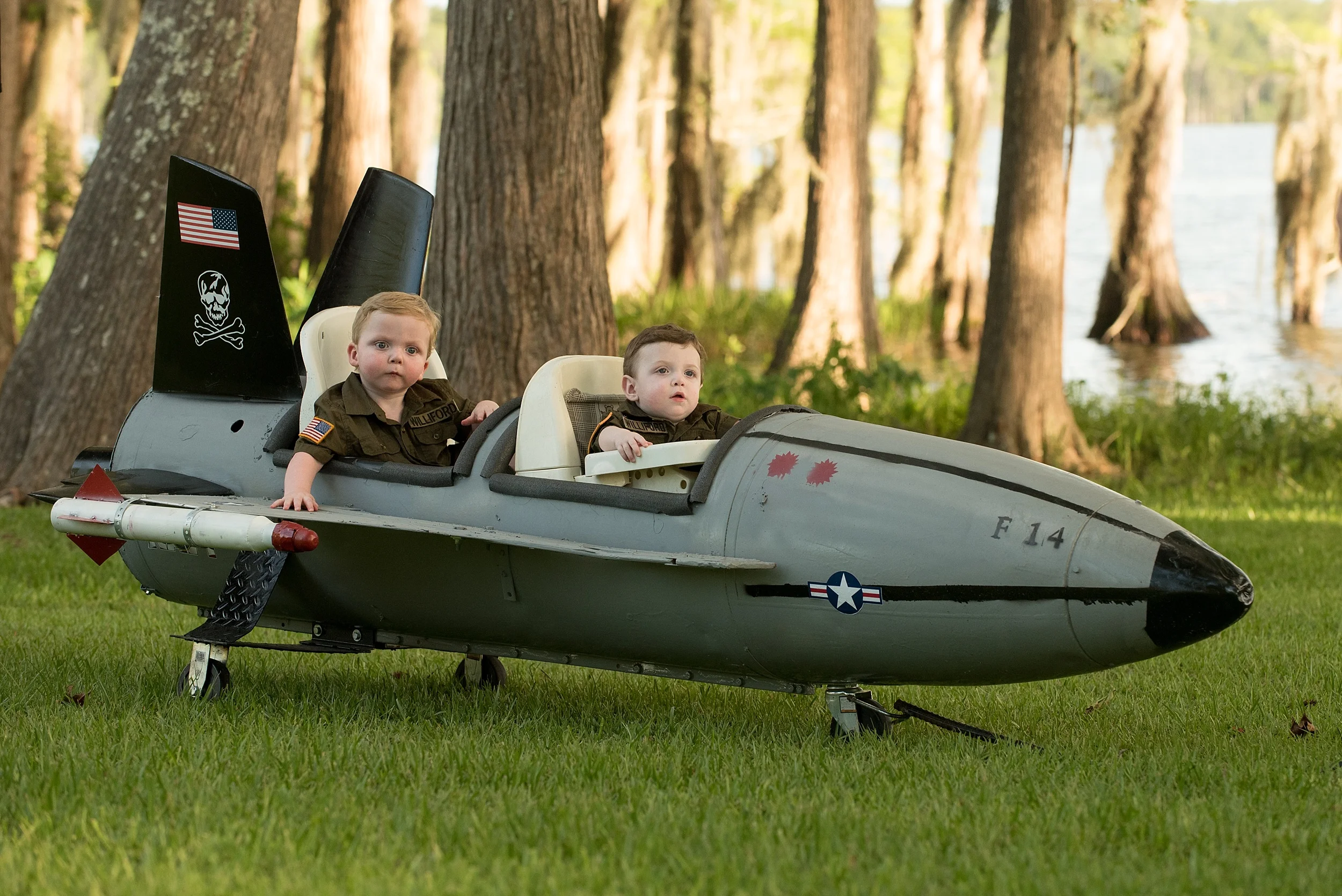 infant brothers sit in toy fighter jet that their dad built