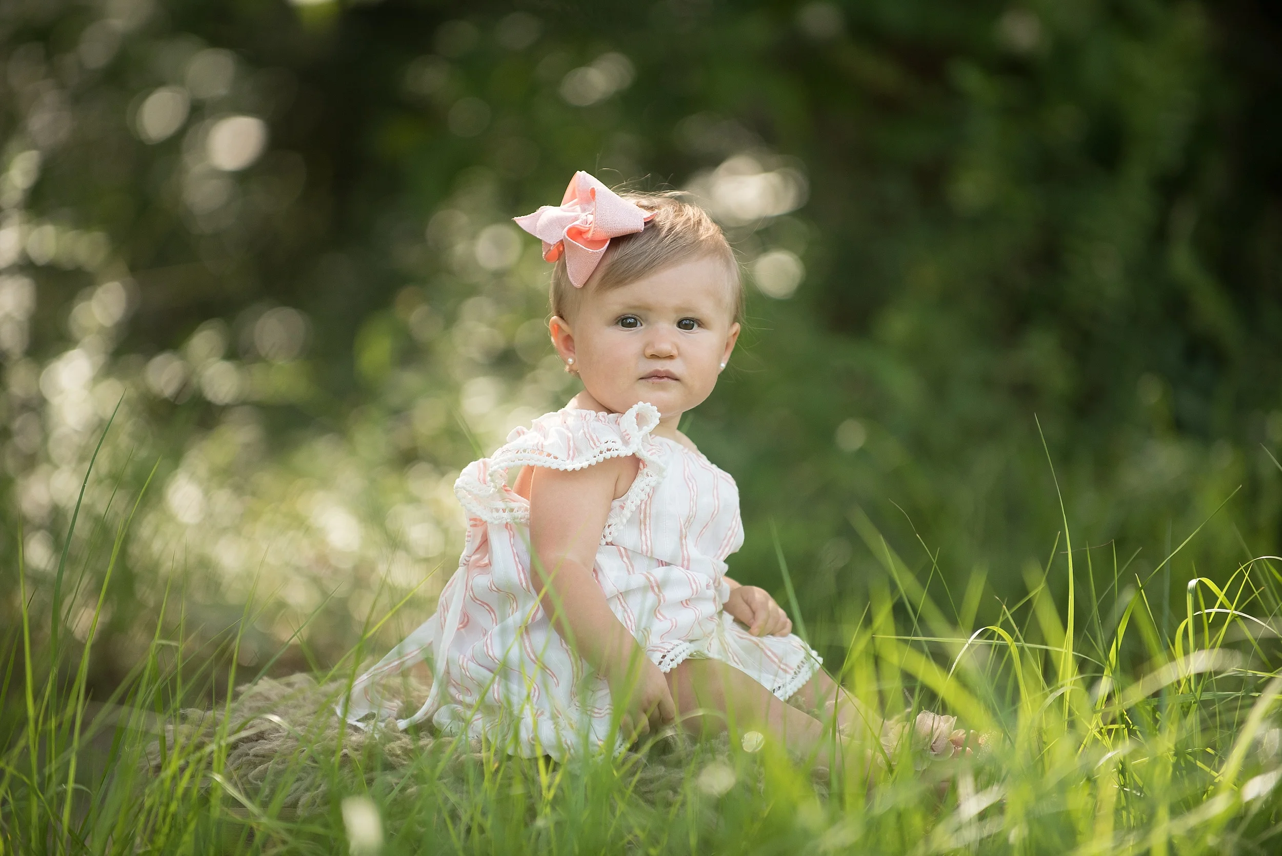 one year old girl with pink bow in a beautiful green outdoor setting