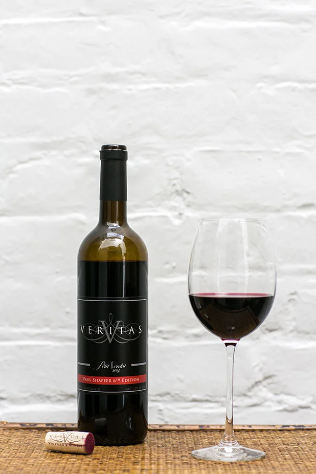 Product photography by Sarah Der of Veritas Winery petite verdot 6th edition bottle with glass of wine and cork.