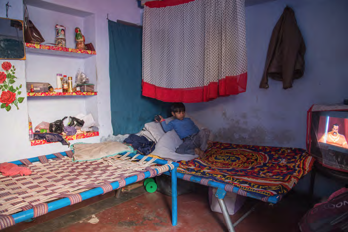 Shari is going to school. After school he loves watching cartoons like every child. He is sharing his bed with his older brother, who is working very late everyday. His father is working too and his mother is taking care of a few kids in the neighbourhood in the afternoons who are not attending school.