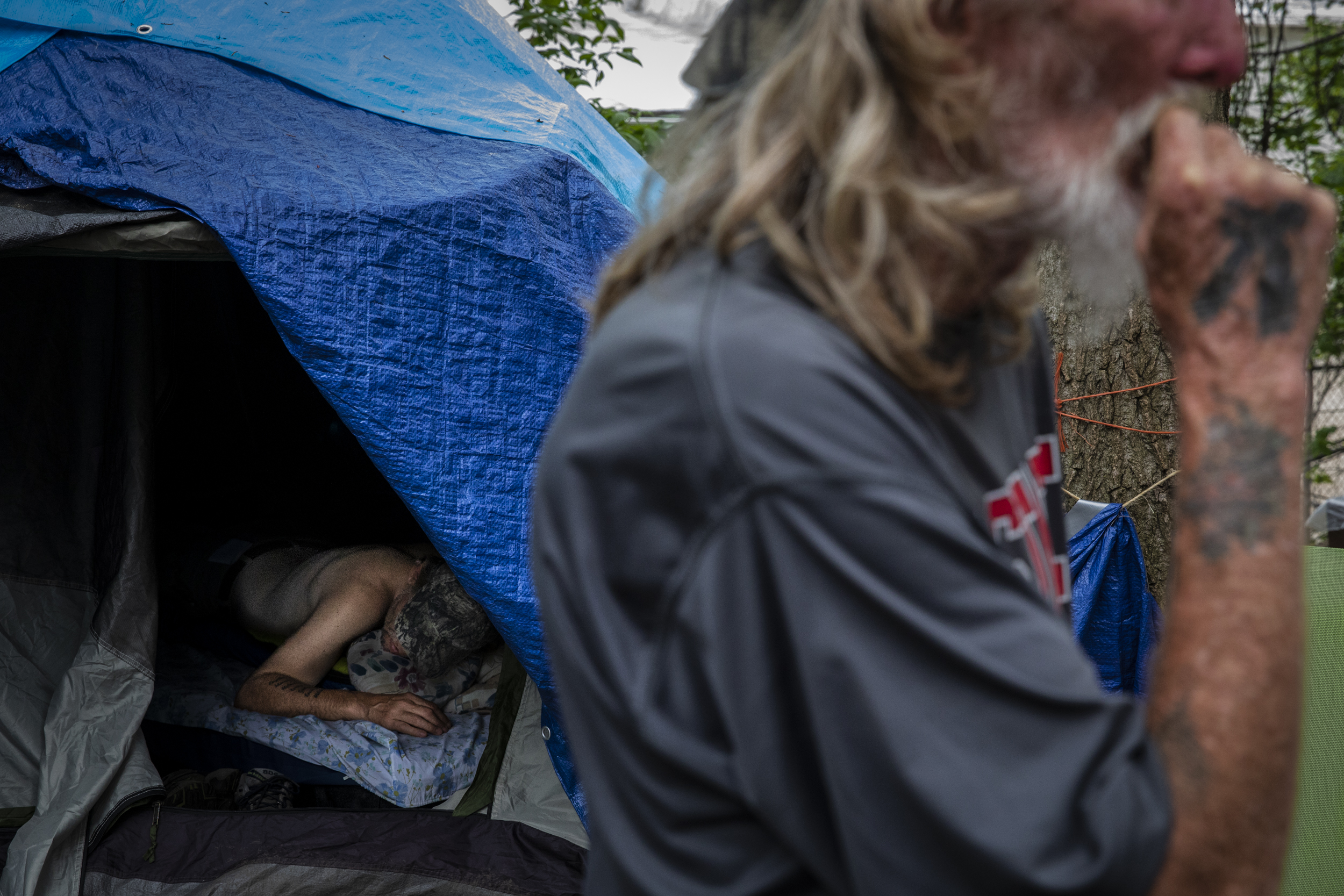 Kevin, who is legally blind and suffers from seizures, sleeps in his tent, while Willie stands outside talking to other residents. Both have been residents of Tent City for over six months, though neither make any attempts to find permanent housing.