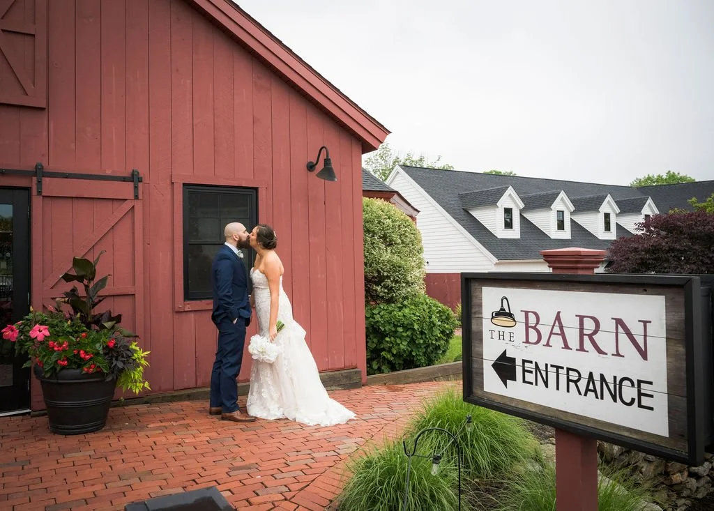 Kelley and Daveed outside the red barn beside The Barn entrance sign