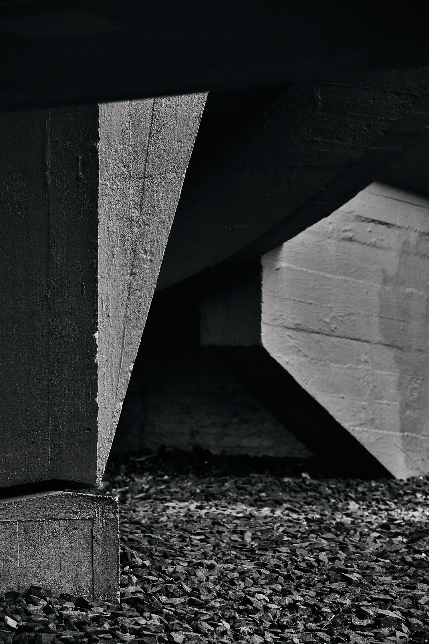Close-up of black and white concrete parts under a bridge on a gravel floor.