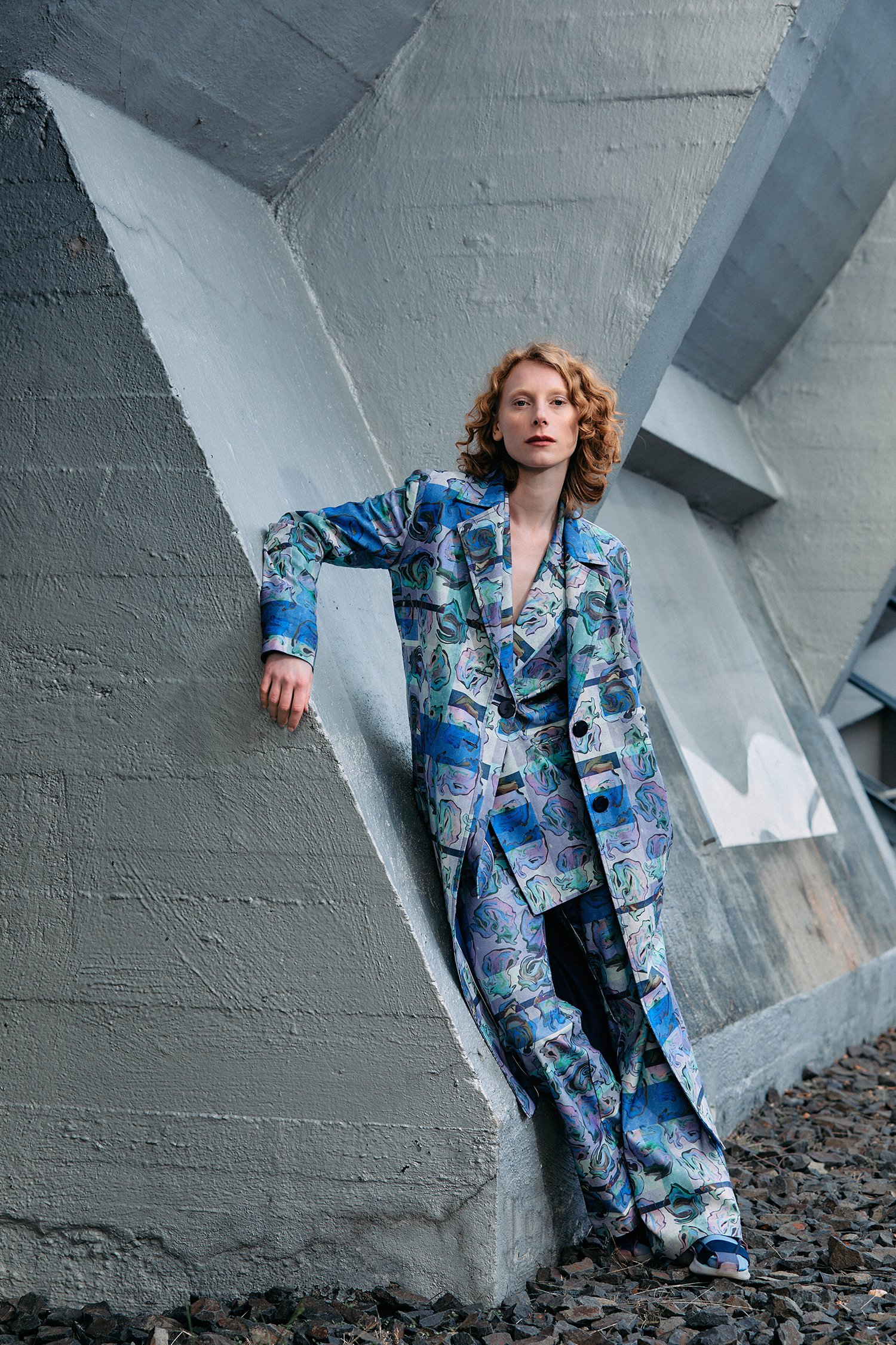 Woman in a colorful, patterned suit stands in front of a modern, geometric concrete wall.