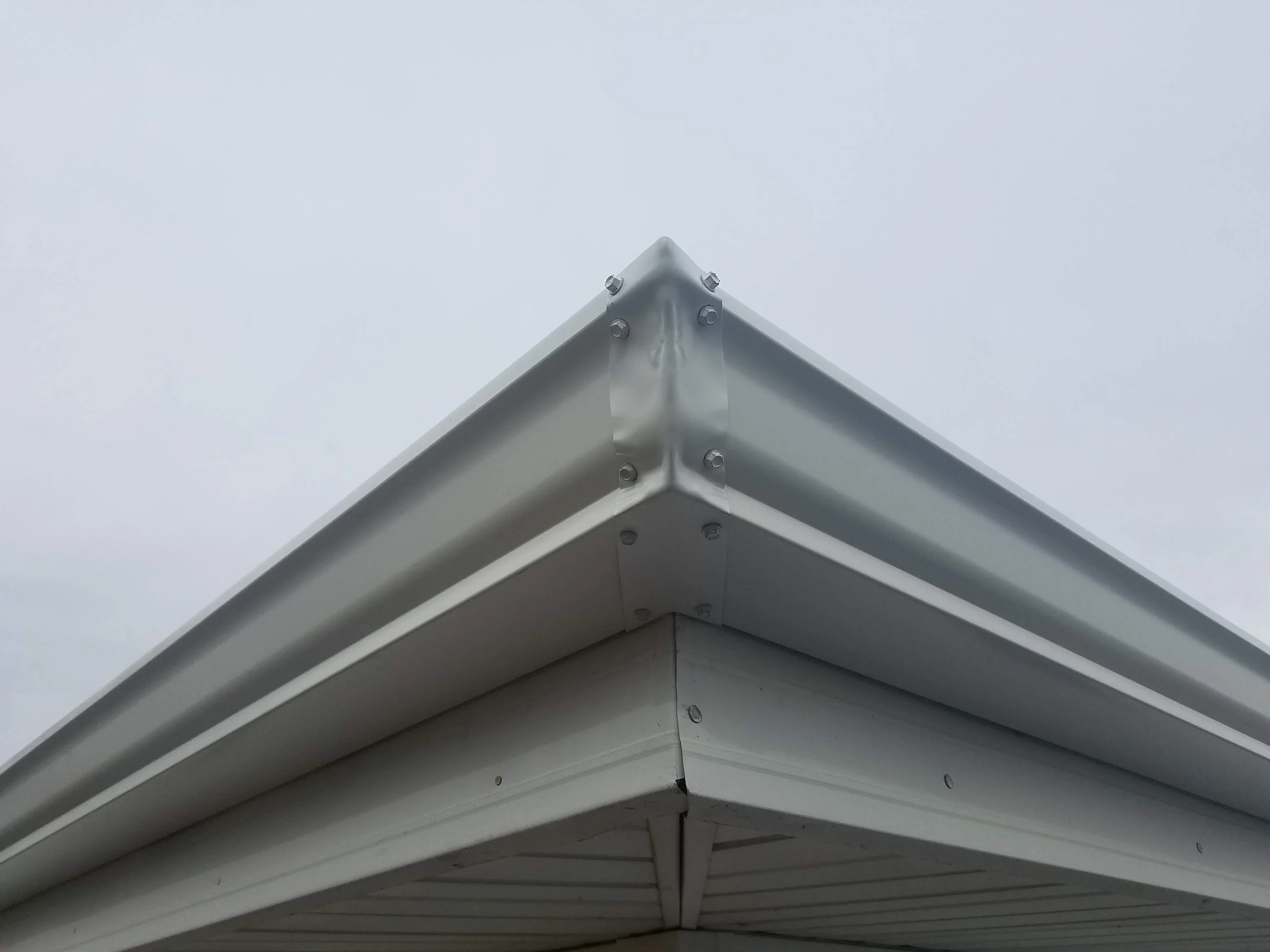 Close-up of the corner of a metal building roof with visible fasteners against a cloudy sky.