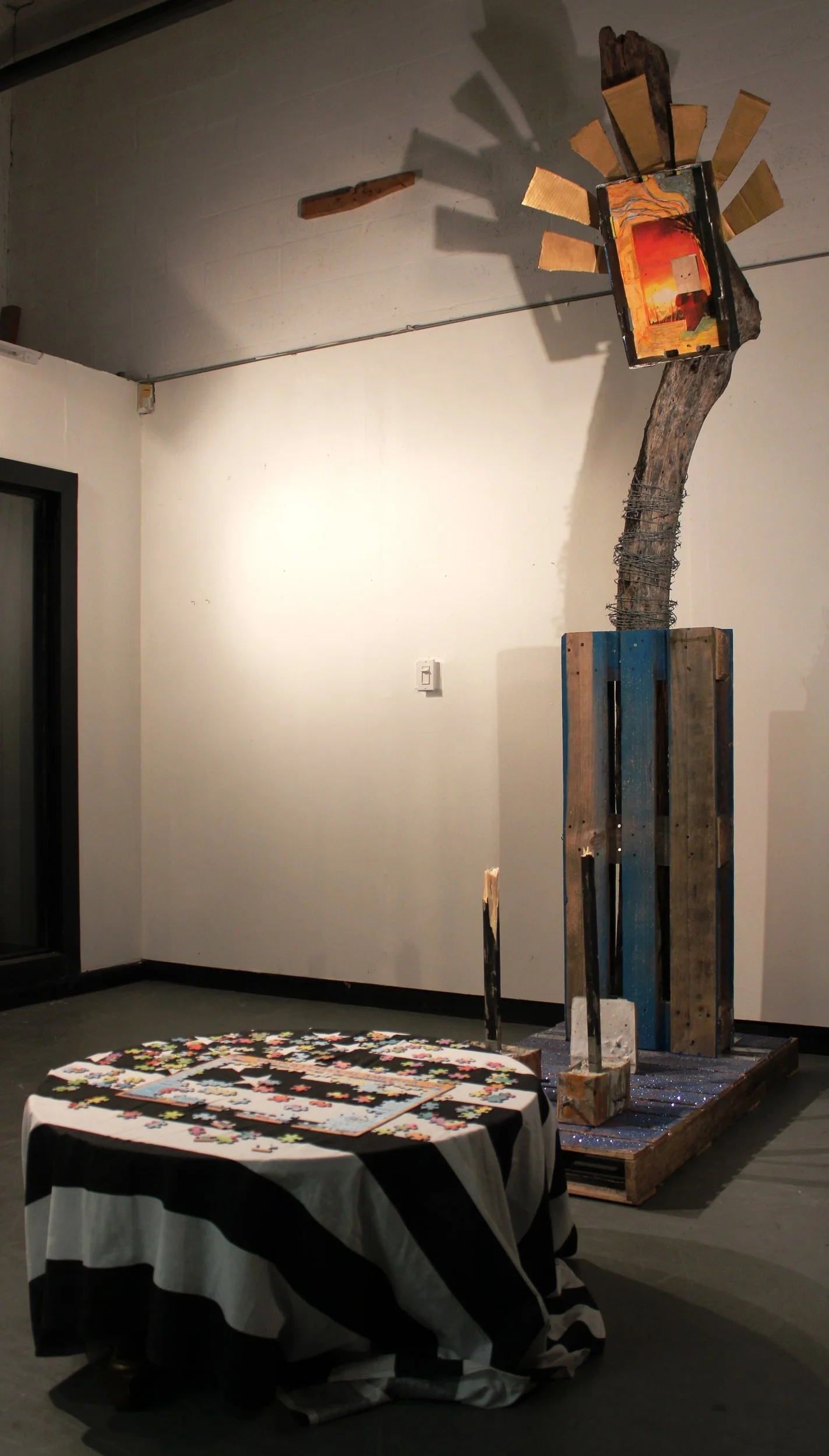  Ofrenda  October 2017  Found objects, black and white American flag, coffee table, jigsaw puzzle of the United States of America, palettes, glitter, glue, concrete shoes in card board boxes with rebar and 1’x2” black painted woods, concrete plaque, 