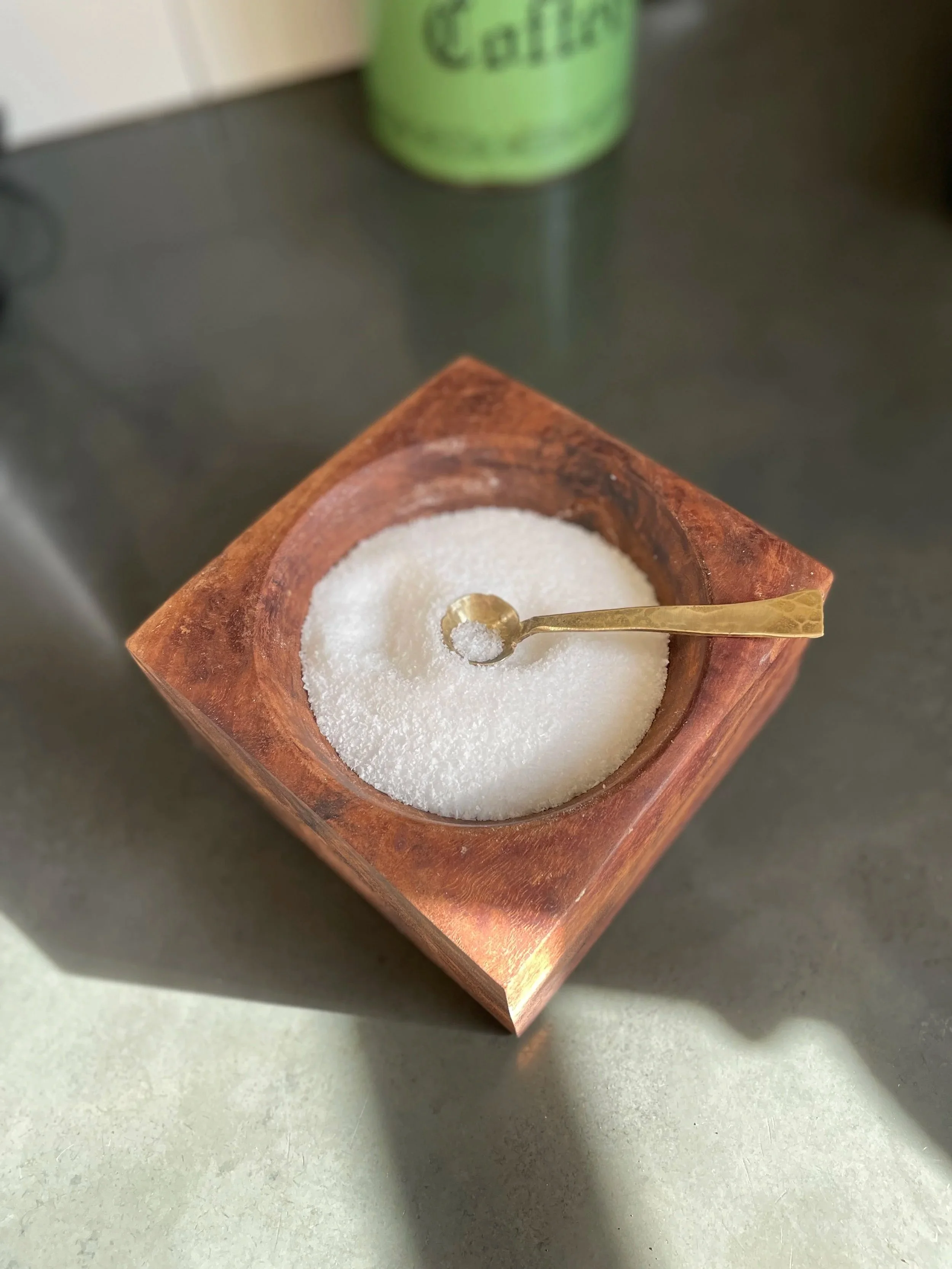 A wooden bowl filled with salt with a small brass spoon resting in it.