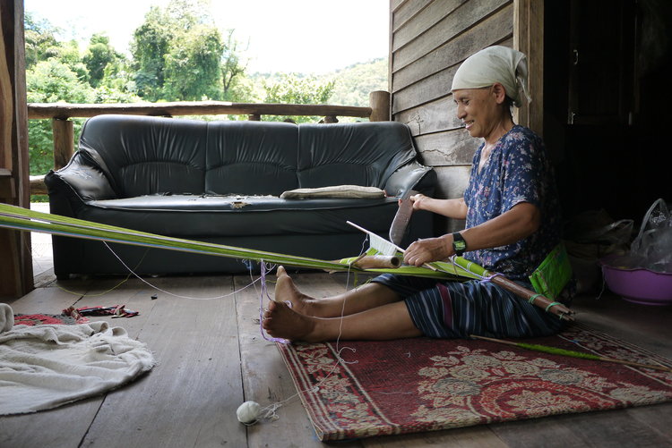 A weaver working on her house balcony, with a backstrap loom in Mae Takri, Doi Saket District, Chiang Mai Province. Photo by Sali Sasaki.