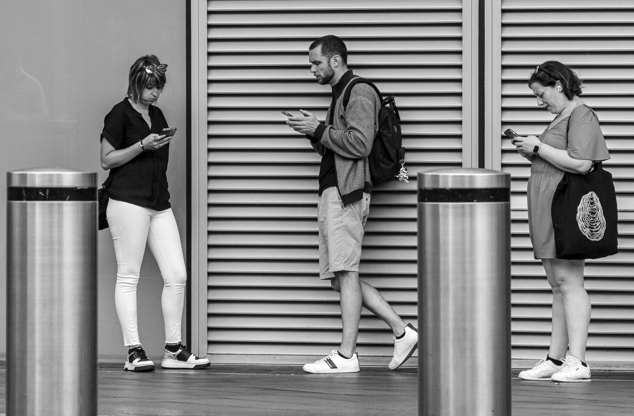 Steve Preston - Posts - Outside London King's Cross. The 3 on their phones, behind the posts, caught my eye  An unmissable moment.  Canon EOS R7, RF-S18-150mm,129mm, 1/800, f/7.1, ISO 1600
