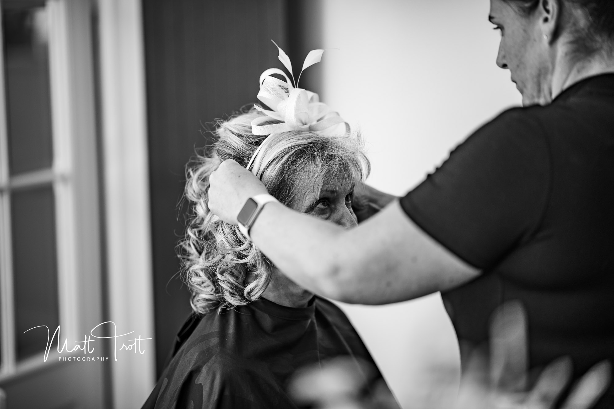 Bridal preparation with the mother of the groom having her fascinator added to her hair
