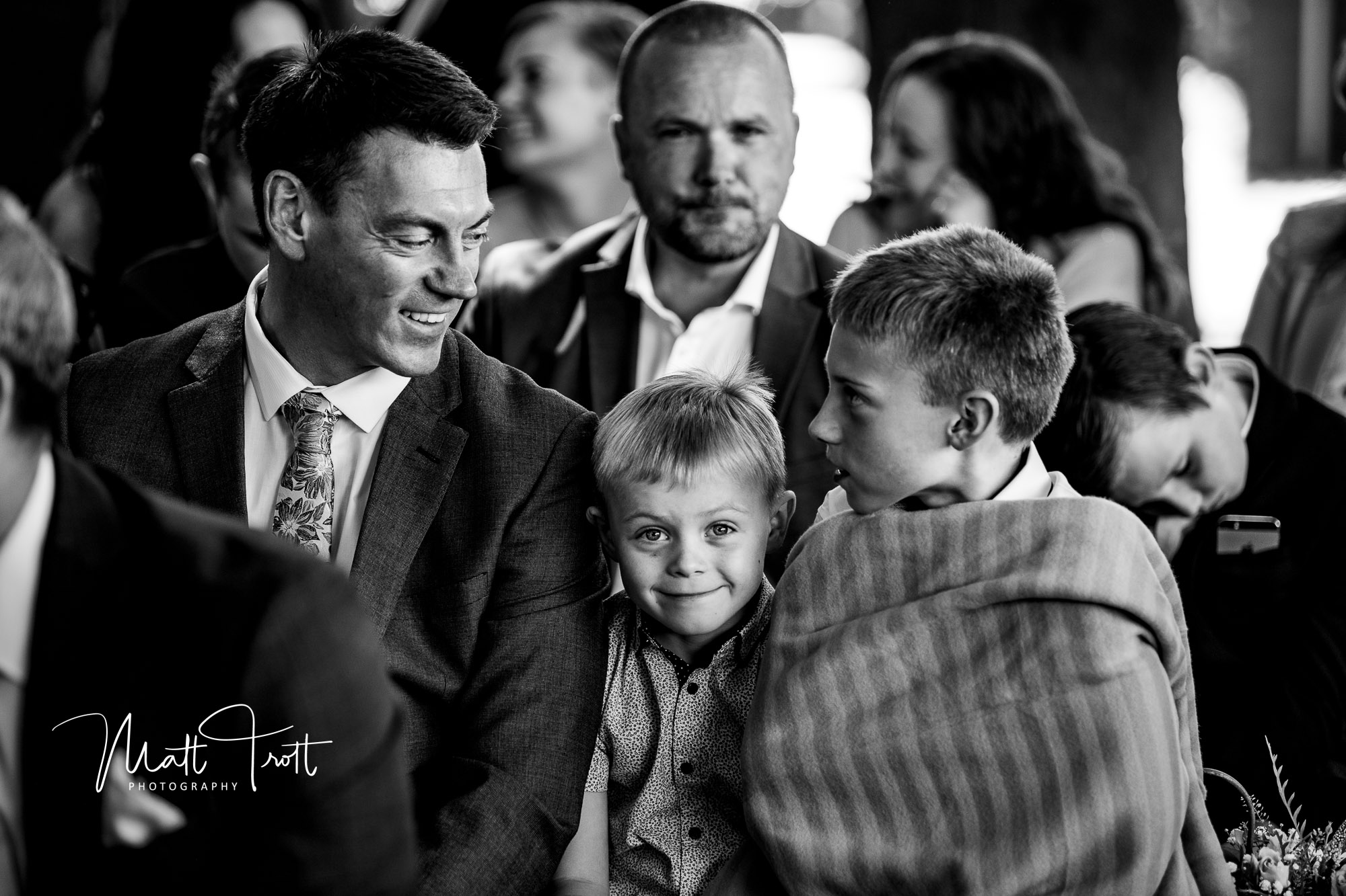 cheeky young boy smiling between his dad and brother whilst waiting for the bride