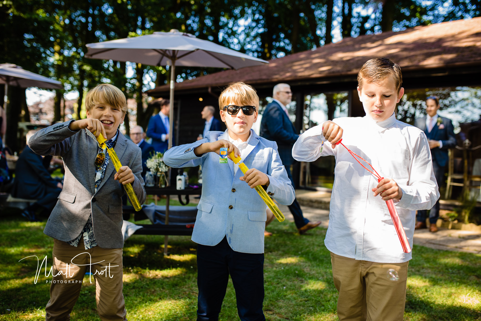 Three young boys blowing bubbles at the camera during a wedding