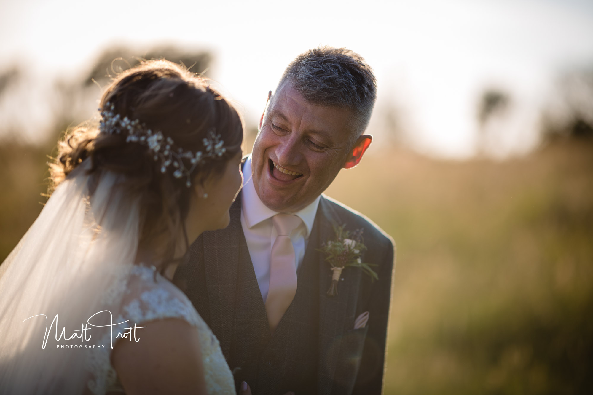 Groom laughing with bride as they walk across a field during their wedding day