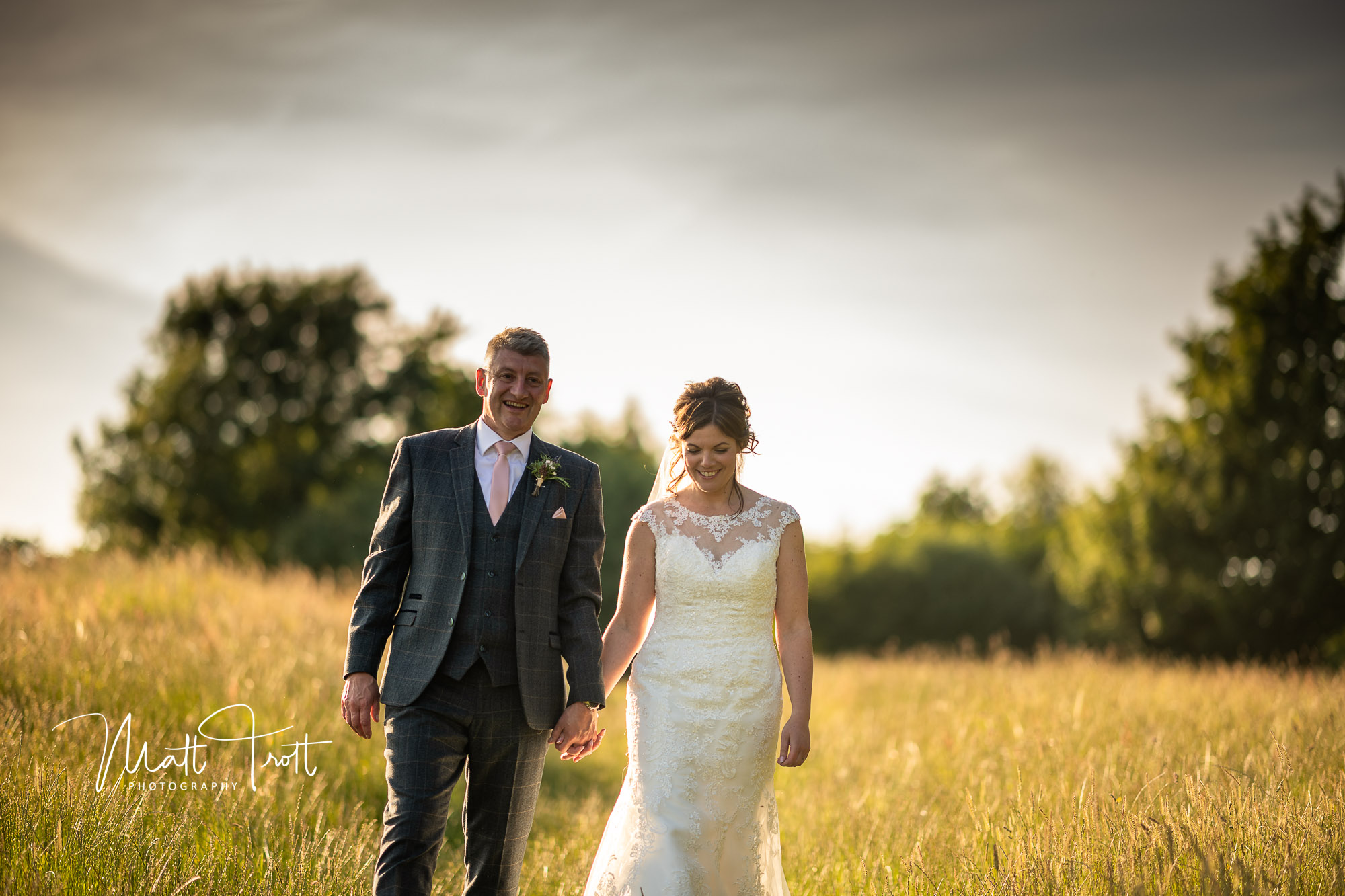 Husband and wife walking through the grass during sunset at crown lodge kent